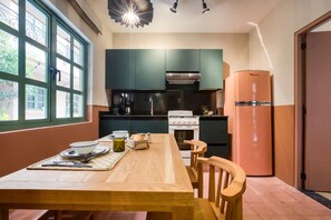 A compact kitchen with dark cabinets, a white stove, and a pink refrigerator. A wooden table with chairs is set for dining.