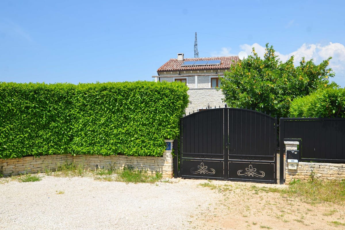 A house with a tiled roof, a black gate, and a hedge in front.