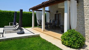 Une terrasse extérieure couverte, avec un bâtiment en pierre, un coin repas comprenant des chaises et une table, et un petit jardin.