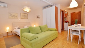 Una stanza piccola e luminosa con un divano verde, un letto, un tavolo da pranzo con sedie e un angolo cottura.