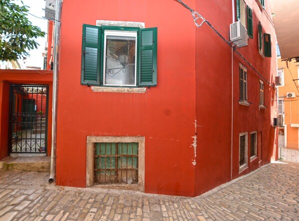 Un edificio rojo con contraventanas verdes, una reja metálica y una calle adoquinada.