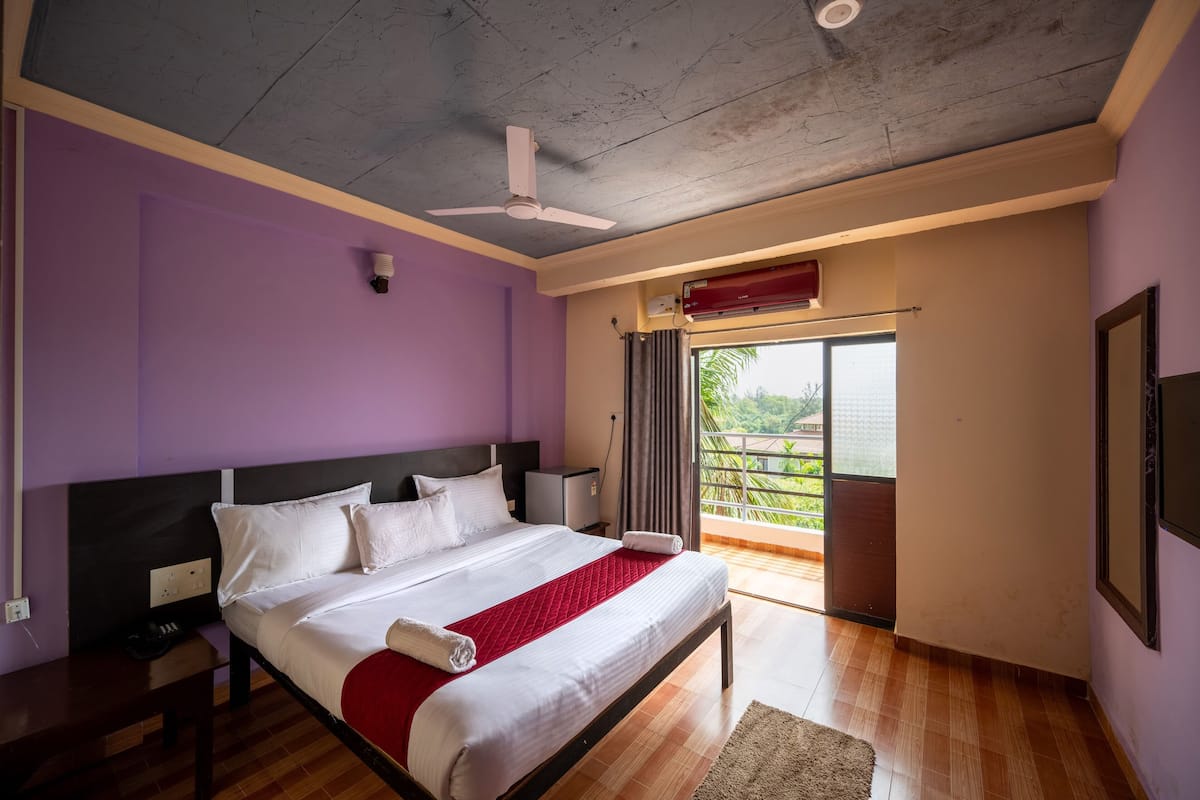 A modern bedroom with a large bed, a ceiling fan, a window with curtains, and a view of greenery outside.