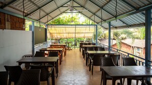 A covered outdoor dining area with tables and chairs, a ceiling fan, and a view of the surrounding buildings. - Shree Rajeshwari Resort  (Morjim)