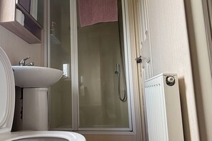 Ett badrum med ett vitt handfat, en duschkabin med glasväggar och en handduk som hänger på duschdörren.