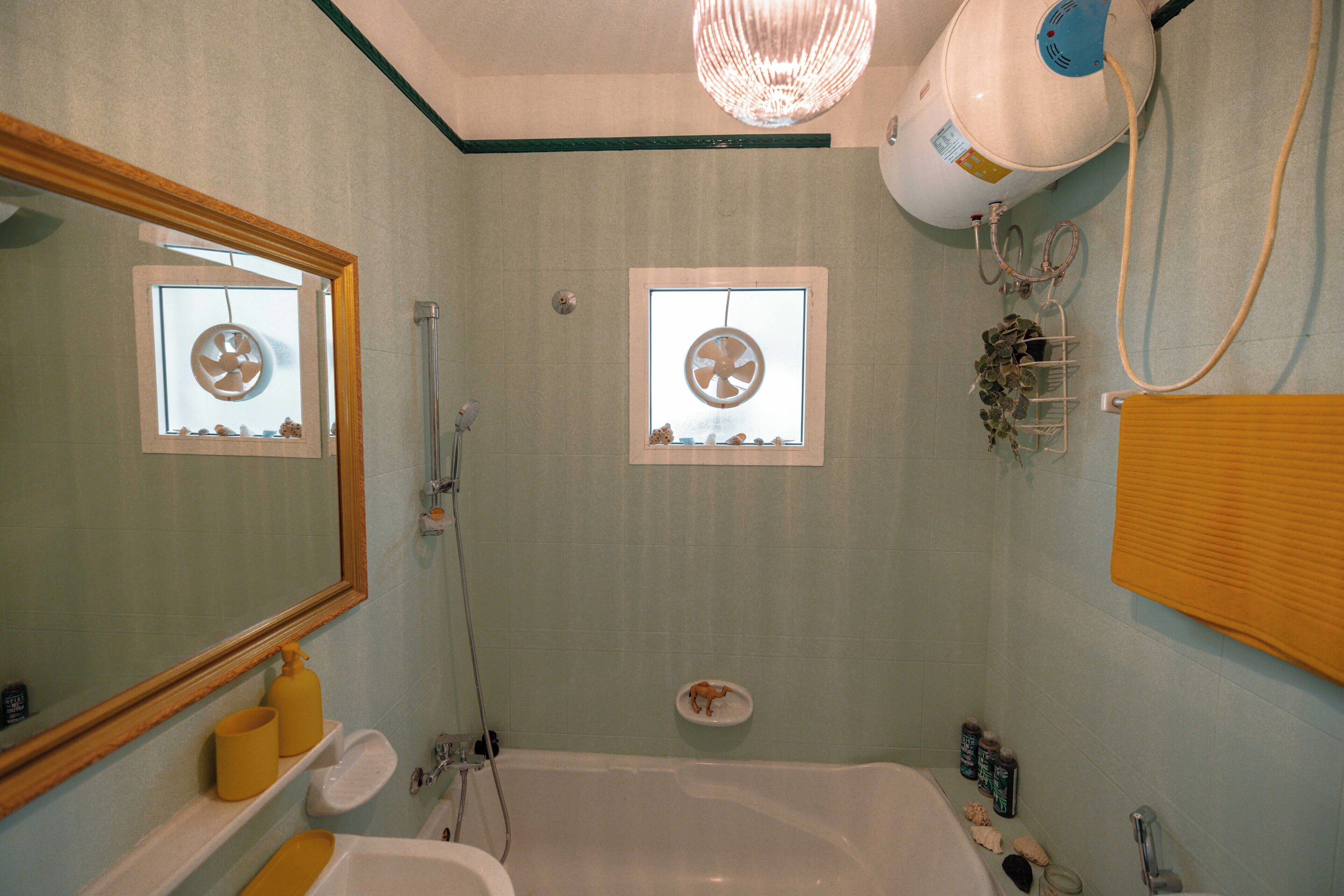 Un baño con bañera, un espejo grande y una ventana con ventilador.