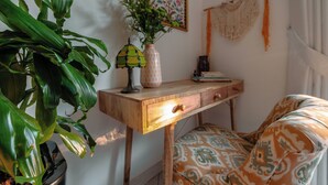 Une pièce avec un bureau en bois, un fauteuil à motifs, une plante en pot, un vase de fleurs et une décoration murale.
