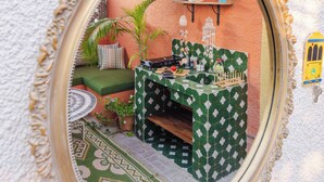 Un espace extérieur accueillant, aménagé avec une table à motifs verts, un banc en bois et un petit jardin agrémenté de plantes en pot.