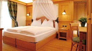 A room with a wooden bed, a nightstand, a chair, and a small table with a plant. - Nivis Hotel  (Dimaro Folgarida)
