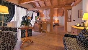 A cozy, rustic room with wooden beams, a wooden dining table, floral-patterned sofas, and a television. - Nivis Hotel  (Dimaro Folgarida)