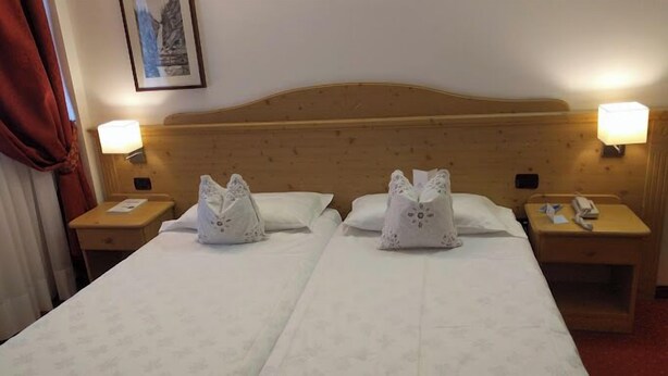 A double bed with two decorative pillows, wooden headboard, bedside lamps, and a framed picture on the wall. - Nivis Hotel  (Dimaro Folgarida)