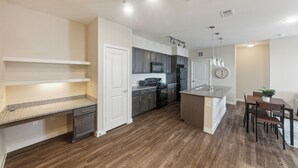 A modern kitchen with wooden flooring, built-in cabinets, a central island, and pendant lighting. - Cullen 5312 I New Construction 2Bd Apt I Gated (Houston)