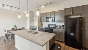 Une cuisine moderne dotée de plans de travail en granit, d’appareils électroménagers en acier inoxydable et de luminaires suspendus.