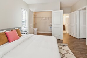 Ein Hotelzimmer mit Bett, Nachttisch, Lampe, Kleiderschrank und einem durch eine offene Tür einsehbaren Badezimmer.
