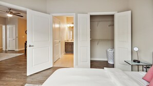 Ett sovrum med en stor säng, ett nattduksbord med en lampa och en öppen garderob.