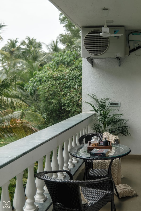 A balcony with a glass table, wicker chairs, and a potted plant.