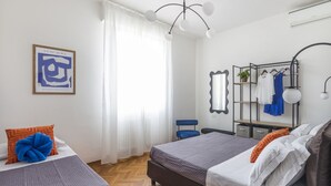 Un dormitorio con dos camas, un candelabro colgante, un espejo, un perchero y una obra de arte enmarcada en la pared.