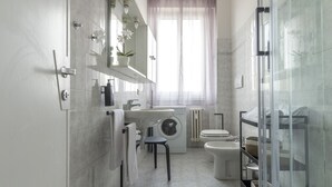 Une salle de bain moderne équipée d’un lavabo, de toilettes, d’une douche et d’un espace douche clos par des parois de verre.