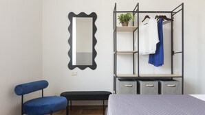 Un dormitorio con cama, una silla, un banco y un armario, además de un espejo.