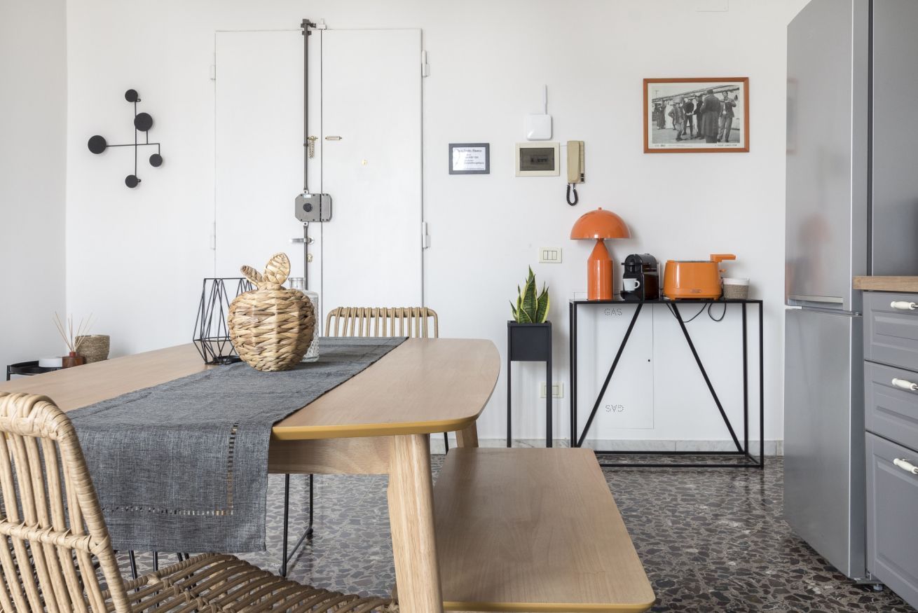 Eine moderne Küche mit Esstisch, Stühlen, einer Bank, einer Kaffeemaschine, einer Pflanze und einem gerahmten Bild an der Wand.