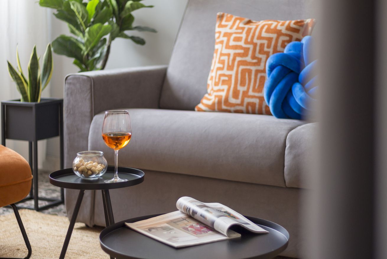 Een moderne woonkamer met een bank, een drankje, een schaal met noten en een krant op een bijzettafeltje.