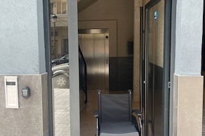 Ein Eingangsbereich mit Glastür, einem Wandintercom und einem Aufzug im Hintergrund.