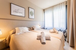 A hotel room with two beds, a bedside table, a lamp, and a window with curtains. - STANDARD APARTMENT IN VALENCIA (València)