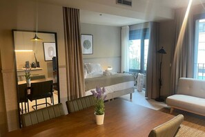 A hotel room with a bed, a dining table with chairs, a sofa, a desk with a chair, a lamp, and a window with curtains. - STANDARD APARTMENT IN VALENCIA (València)