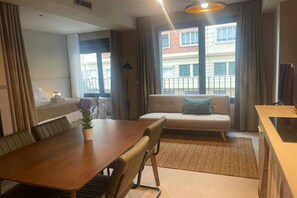 A hotel room with a dining table, chairs, a sofa, a small kitchen area, and a large window with curtains. - STANDARD APARTMENT IN VALENCIA (València)