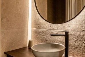 A bathroom with a large round mirror, a modern sink, and a textured wall.