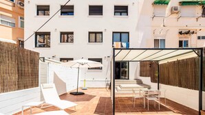 A courtyard with white lounge chairs, a covered seating area, and a building with multiple windows in the background.