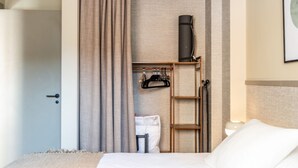 A hotel room with a bed, a wardrobe, a ladder, a hanging coat rack, and a wall-mounted heater.