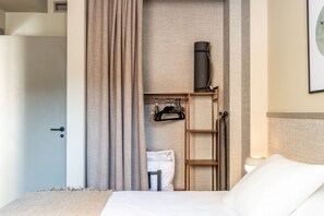 A hotel room with a bed, a wardrobe, a ladder, a hanging coat rack, and a wall-mounted heater.