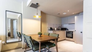 A modern kitchen with a dining area, featuring a wooden table, green chairs, and a pendant light.