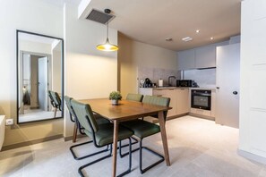A modern kitchen with a dining area, featuring a wooden table, green chairs, and a pendant light.