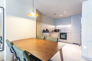 Une cuisine moderne avec des meubles blancs, une table à manger en bois et des chaises recouvertes d’un tissu vert.