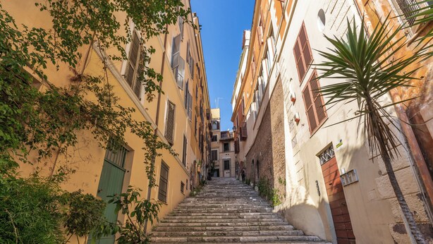 A narrow, stone staircase leading up to a building entrance, surrounded by yellow buildings with shutters and greenery. - CIANCALEONI APPARTAMENTO (Rome)