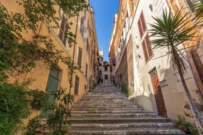 Una stretta scala in pietra conduce all'ingresso di un edificio, circondato da edifici gialli con persiane e vegetazione.