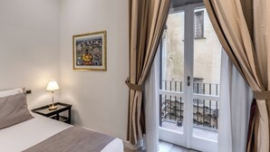 A hotel room with a bed, a nightstand with a lamp, a framed picture on the wall, and a balcony with curtains. - CIANCALEONI APPARTAMENTO (Rome)