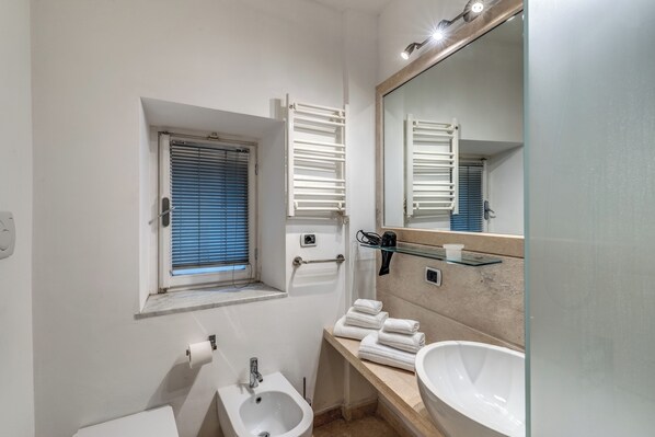 Un bagno moderno con bidet, lavabo, specchio e finestra con persiane.