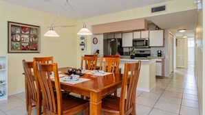 A dining area with a wooden table and chairs, a kitchen in the background, and a clock on the wall. - Villas at Island Club Community, Pools, Jacuzzi and More! (Kissimmee)