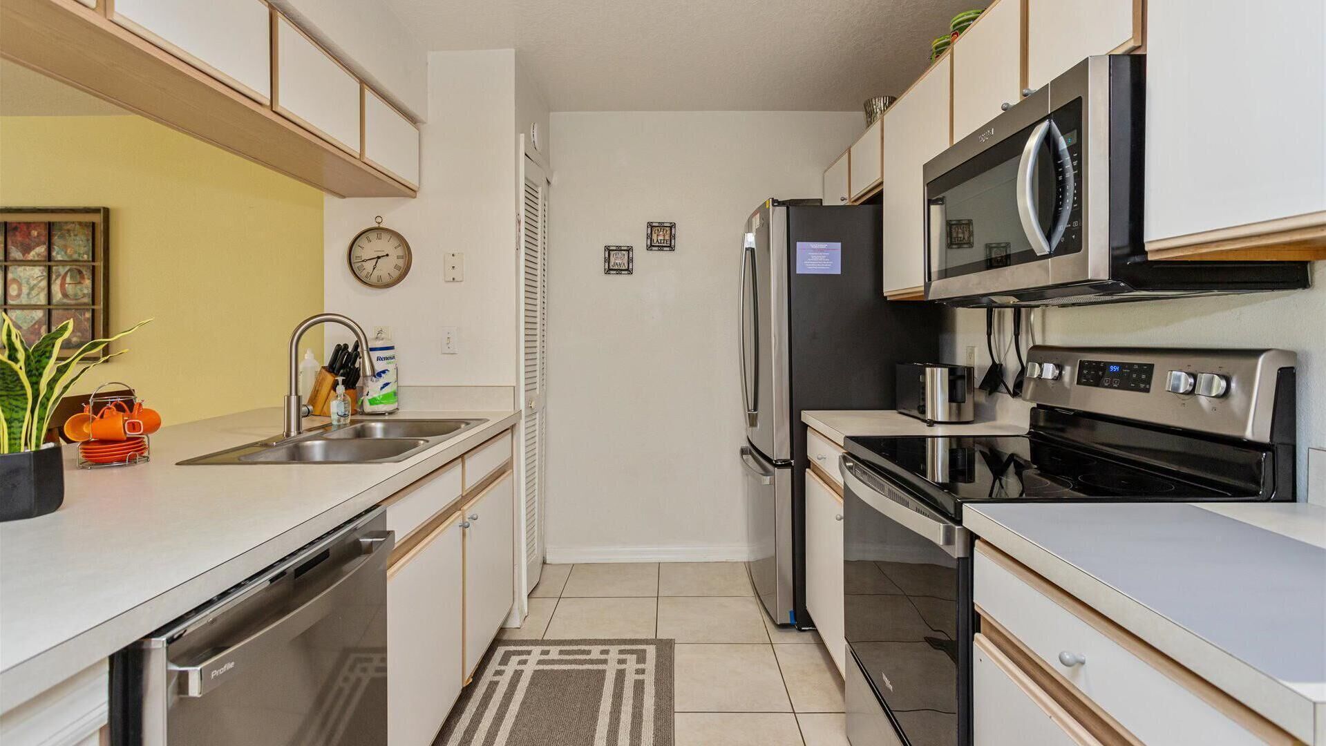 A modern kitchen with stainless steel appliances, a sink, and a clock on the wall.
