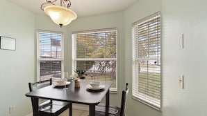 A dining area with a table set for two, two chairs, a chandelier, and a window with blinds. - Cozy Home Near Disney!!! (Kissimmee)