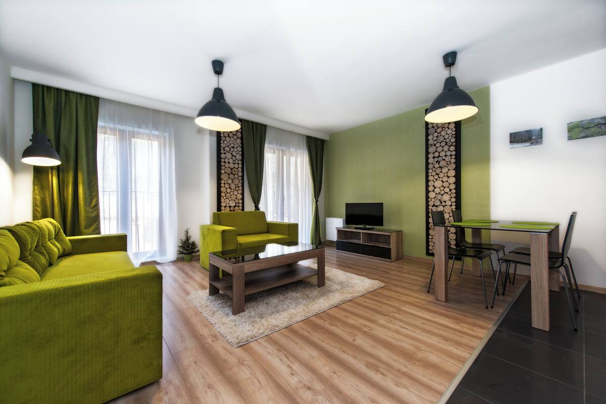 Una sala de estar moderna con un sofá verde, una mesa de centro, un televisor y un comedor con mesa y sillas.