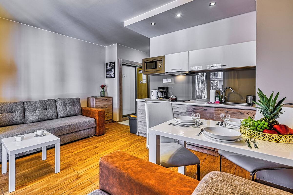Una sala de estar moderna con sofá, mesa de centro y comedor, con cocina al fondo.