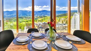 Una mesa de comedor preparada para seis personas, con vistas a un paisaje montañoso a través de amplios ventanales.