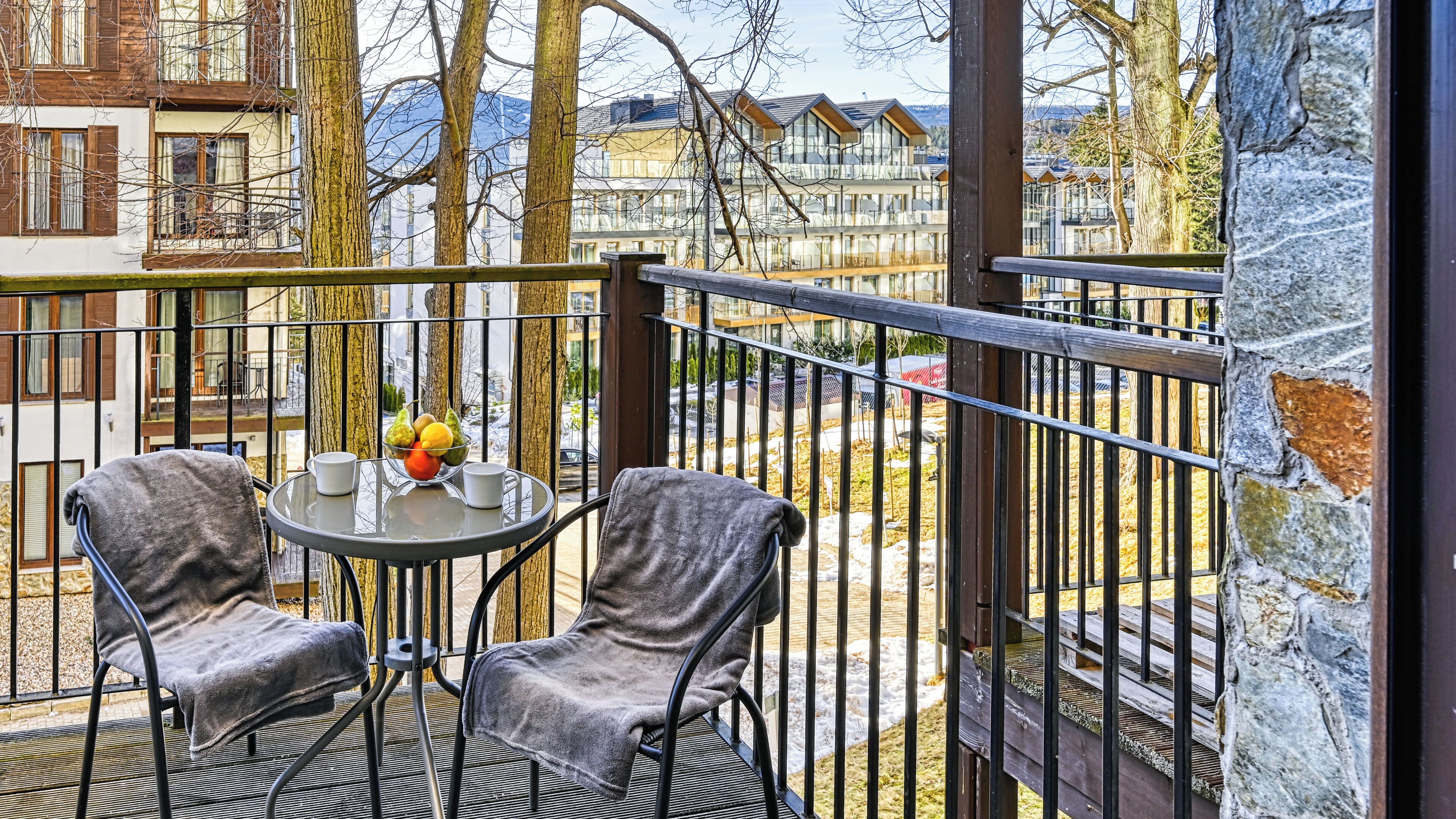 A balcony with two chairs and a table, a bowl of fruit, and a vase of flowers.
