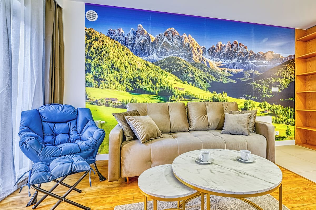 Una sala de estar con un sofá, un sillón azul, una mesa redonda con dos sillas y una estantería.