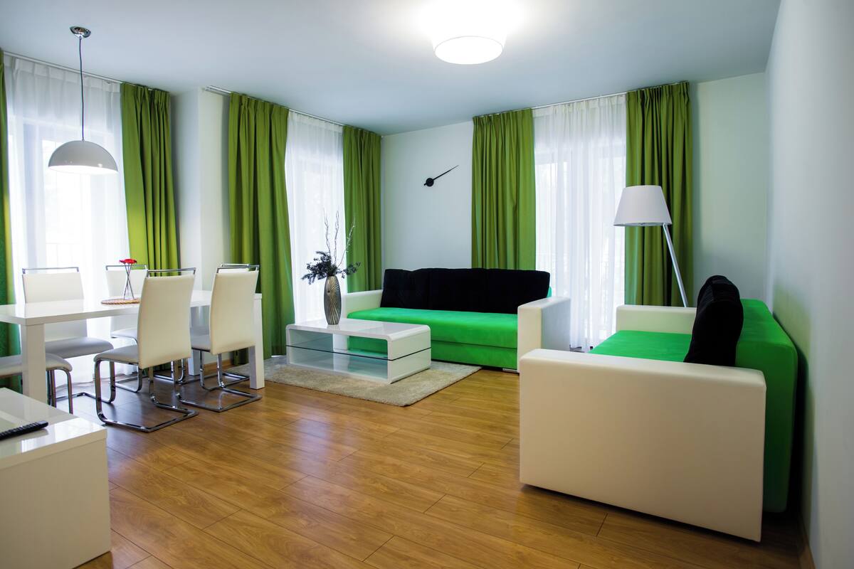 Una sala de estar moderna con un sofá verde, sillones blancos, una mesa de centro y una zona de comedor con una mesa y sillas blancas.