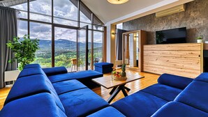 Una sala de estar moderna con ventanas amplias, un sofá azul, un mueble de madera y vistas a las montañas.