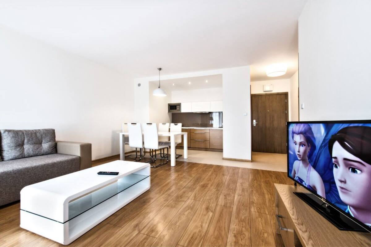Una sala moderna con un sofá, una mesa de centro, un televisor y un comedor con sillas y una mesa.